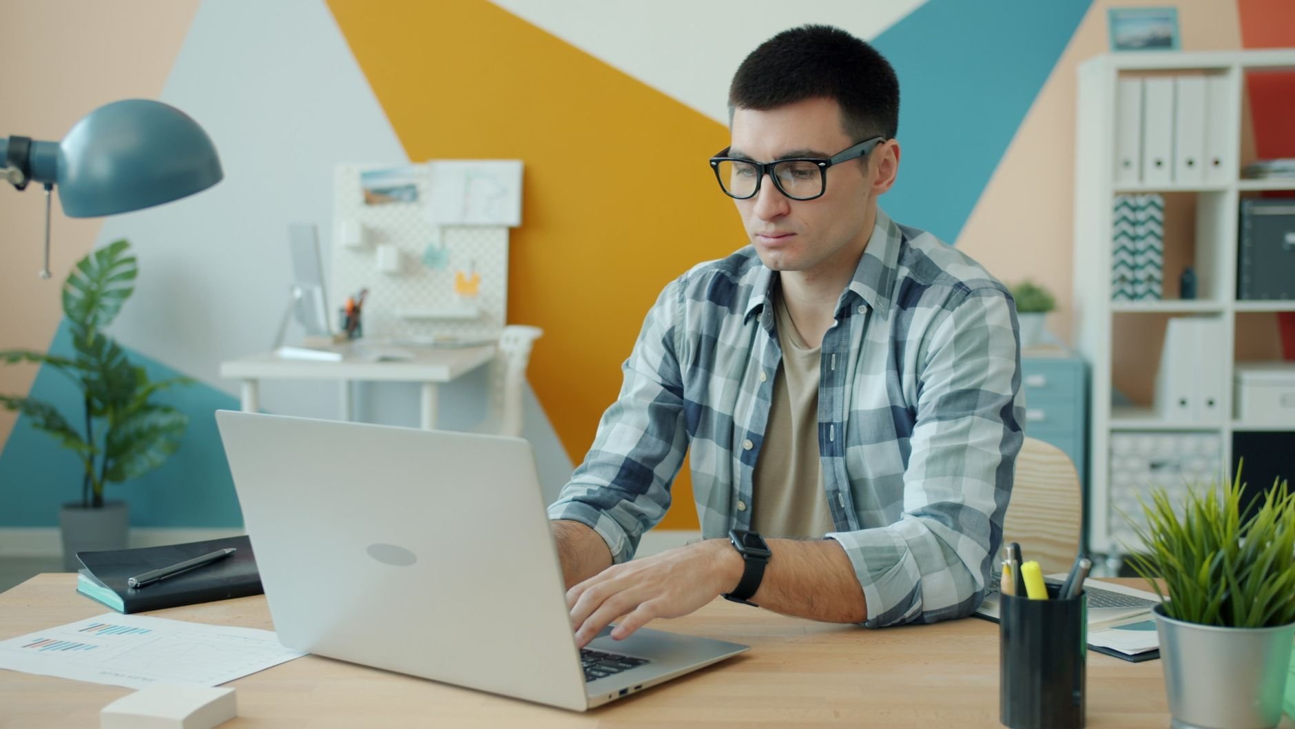 Focused young man wearing glasses, working on a laptop in a stylish office.